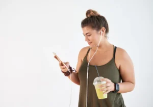 A woman is holding her phone and drinking juice.