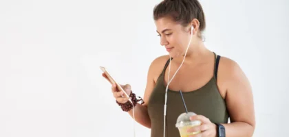 A woman is holding her phone and drinking juice.