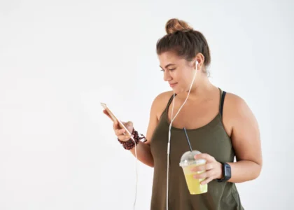 A woman is holding her phone and drinking juice.