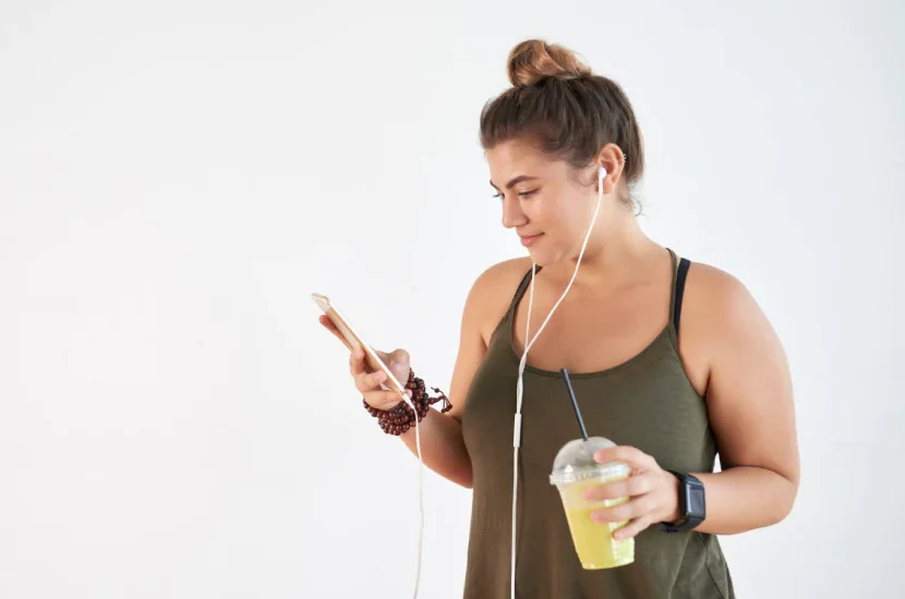 A woman is holding her phone and drinking juice.