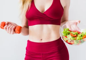 A woman holding a bowl of salad and a carrot.