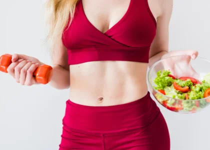 A woman holding a bowl of salad and a carrot.