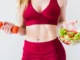 A woman holding a bowl of salad and a carrot.