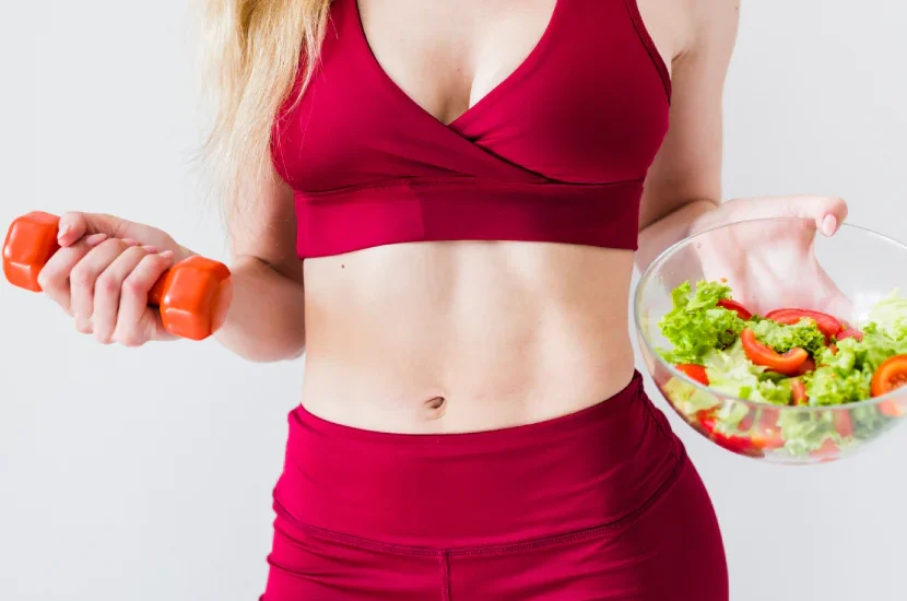 A woman holding a bowl of salad and a carrot.