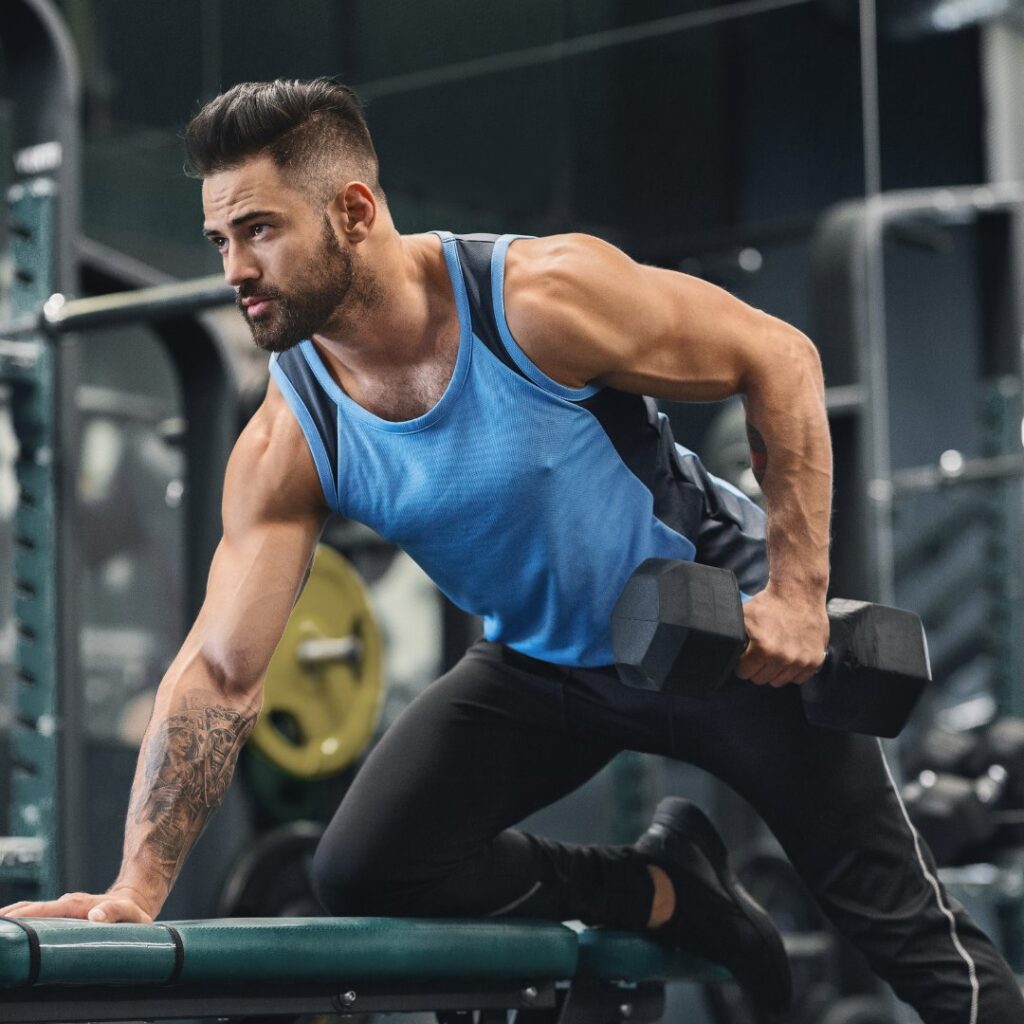 A man is holding a dumbbell while standing in the gym.